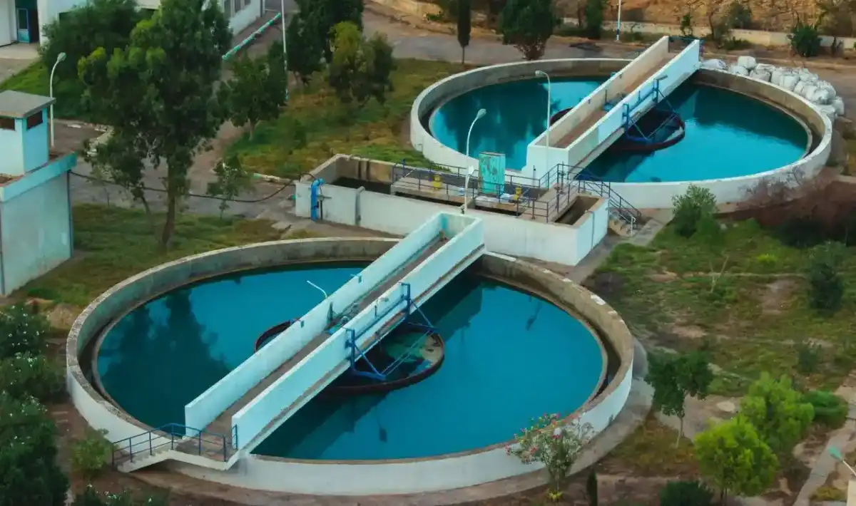Uma fotografia aérea mostra uma estação de tratamento de esgoto com dois grandes tanques circulares utilizados para o tratamento biológico de águas residuais. A instalação processa esgoto de fontes residenciais e comerciais para garantir que a água seja segura para reutilização ou lançamento no meio ambiente.